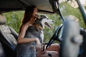 une magnifique Jeune femme est assis derrière le roue de sa voiture ensemble avec une rauque race chien et sourit gaiement jouit le périple photo