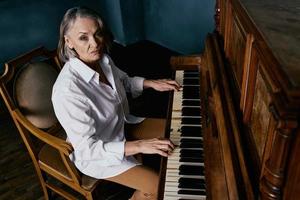 une femme dans une blanc chemise est assis sur une chaise suivant à une piano apprentissage la musique photo