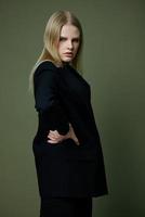 une professionnel blond modèle détient sa taille avec tous les deux mains demi-tourné regards à le caméra posant sur une vert Contexte dans le studio photo