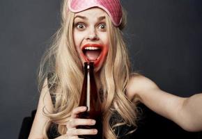 ivre femme avec une bouteille de Bière sur une gris Contexte gestes avec sa mains et brillant maquillage photo