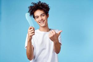 émotif homme avec une peigne dans le sien main et frisé cheveux dans une bleu Contexte copie espace photo