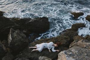 magnifique femme mensonge sur rocheux côte avec des fissures sur rocheux surface vacances concept photo