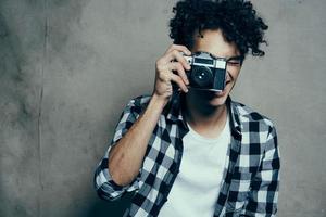 gars avec une caméra dans le sien mains sur une gris Contexte à l'intérieur loisir plaid chemise modèle photo