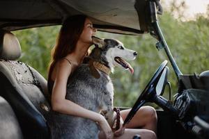 une magnifique Jeune femme est assis derrière le roue de sa voiture ensemble avec une rauque race chien et sourit gaiement jouit le périple photo