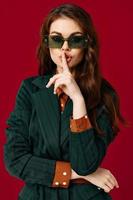 brunette portant des lunettes de soleil détient main près visage luxe rouge Contexte photo