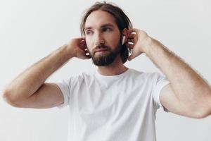 élégant homme dans une blanc T-shirt avec sans fil écouteurs dans le sien oreilles ayant amusement écoute à la musique sourire sur une blanc Contexte mode de vie photo