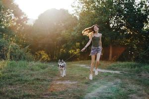 femme et sa rauque chien Heureusement fonctionnement par le herbe dans la nature dans le parc sourire avec les dents tomber marcher avec animal de compagnie, en voyageant avec une chien ami photo