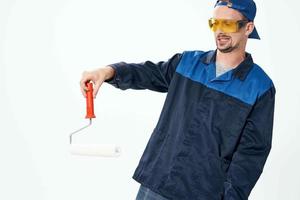 une homme dans une travail uniforme une rouleau pour La peinture des murs dans le sien mains décoration réparation photo