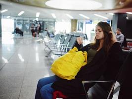 une femme est assis à le aéroport avec une Jaune sac à dos attendre pour une vol photo