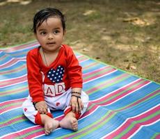 mignonne peu Indien bébé séance profiter Extérieur tirer à société parc dans Delhi, mignonne bébé garçon séance sur coloré tapis avec herbe autour, bébé garçon Extérieur tirer photo