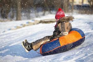 peu enfant sur une traîneau. enfant sur une hiver journée. une garçon est équitation sur une neige glisser. photo