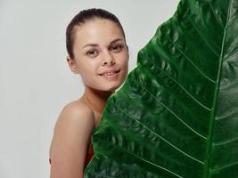 femme en portant vert feuille de paume arbre sur lumière Contexte tondu vue de rouge T-shirt photo