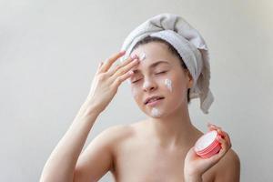 portrait de beauté d'une femme en serviette sur la tête avec un masque nourrissant blanc ou une crème sur le visage, fond blanc isolé photo