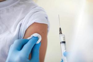 fermer de une enfant est épaule et le mains de une médecin dans médical gants avec un injection pour vaccination. vaccination contre COVID-19 [feminine. photo