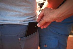 fermer de une homme est main vole une mobile téléphone avec une jeans poche. crime, vol à la tire sur le rue photo