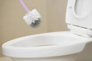 femmes au foyer utilisation une brosse à nettoyer le salle de bains à retirer saleté et prendre se soucier de sanitaire vaisselle. photo