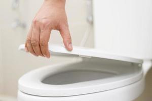 proche en haut main de une femme fermeture le couvercle de une toilette siège. hygiène et santé se soucier concept. photo