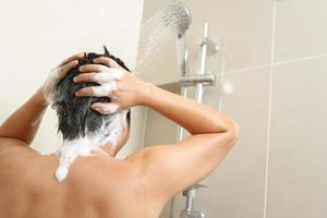 une homme est la lessive le sien cheveux avec shampooing photo