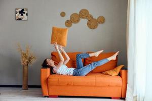 souriant femme sur le Orange canapé dans le du repos pièce posant appartements photo