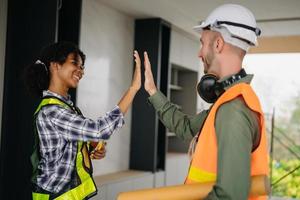 l'équipe de construction se serre la main pour saluer le début d'un nouveau plan de projet derrière un casque jaune sur le bureau du centre de bureau pour consulter son projet de construction. photo