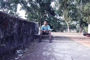 rangpur, bangladesh 2023. déprimé adolescent homme séance seul sur mur dans extérieur.désagréable douleur. triste malheureux Beau homme.bangladeshi et Asie garçon Souffrance dépression. photo