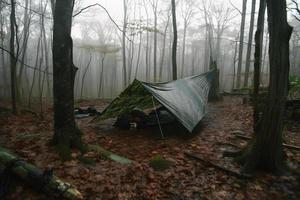 région sauvage survie. bushcraft tente en dessous de le bâche dans lourd pluie, embrassement le refroidissement de aube. une scène de endurance et résistance photo