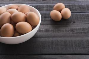 oeufs de poule dans un bol blanc et trois oeufs de poule à l'extérieur sur une table en bois noir photo