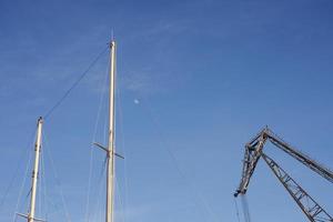 mâts de bateau et une grue contre un ciel bleu avec la lune photo