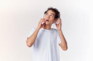 Jeune homme avec écouteurs écoute à la musique Nouveau La technologie blanc T-shirt lumière Contexte photo