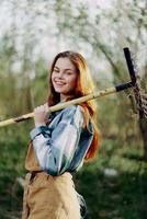 une femme agriculteur dans travail vêtements et un tablier travaux en plein air dans la nature et détient une râteau à recueillir herbe photo