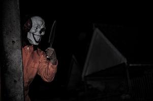 asiatique Beau homme porter pitre masque avec arme à le nuit scène, halloween Festival concept, horreur effrayant photo de une tueur dans Orange tissu