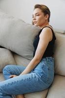 Jeune femme avec court la Coupe de cheveux cheveux ayant amusement à Accueil sur le canapé sourire et bonheur, vacances à maison, Naturel posant sans pour autant filtres, gratuit copie espace photo