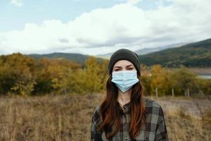 femme dans chaud casquette dans une médical masque dans le l'automne forêt dans le montagnes photo