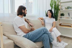 homme et femme copains séance sur le canapé et souriant joyeusement parlant à chaque autre ayant une bien temps ensemble. mode de vie dans bonheur à Accueil photo