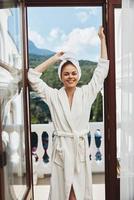 portrait de magnifique femme avec une serviette sur mon tête dans une blanc peignoir de bain rester sur le balcon dans une Hôtel photo