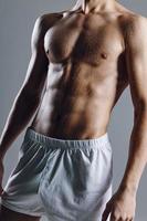 sportif Masculin bodybuilder avec abdos cubes sur estomac gris Contexte blanc short photo
