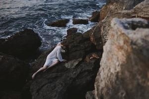 de haut en bas aérien vue de magnifique Jeune femme dans longue blanc robe mensonge sur rocheux côte avec des fissures sur rocheux surface photo