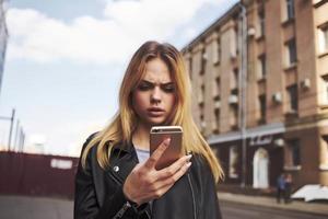 tondu vue de blond femme avec mobile téléphone sur le rue près le bâtiment photo