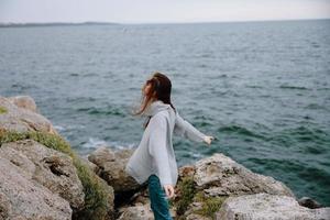 magnifique femme dans une gris chandail des stands sur une rocheux rive la nature mode de vie photo