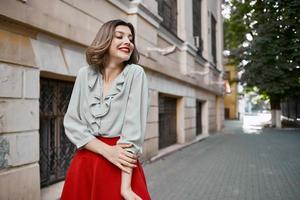 jolie femme dans rouge jupe sur le rue marcher près le bâtiment photo