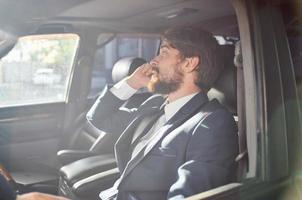 une homme dans une costume est séance dans le voiture et parlant sur le téléphone photo
