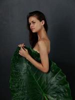 jolie femme avec nu corps est couvert par une grand vert feuille foncé Contexte photo