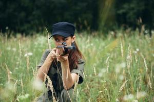 femme sur Extérieur est assis dans une abri avec une arme dans sa mains une Regardez à le côté. vert salopette photo