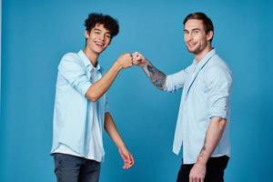 une homme avec une tatouage secoue mains avec une frisé gars sur une bleu Contexte copains la communication photo