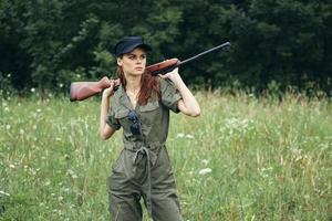 femme sur Extérieur en portant une arme dans le sien mains Regardez de côté chasse vert feuilles photo