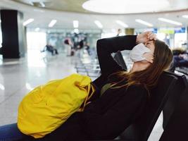 une femme avec une Jaune sac à dos est assis à le aéroport longue attendre pour une vol photo