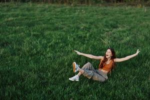 Jeune femme en jouant Jeux dans le parc sur le vert herbe diffusion sa bras et jambes dans différent directions chute et souriant dans le lumière du soleil de été, une mode de vie de la vie et jeunesse photo