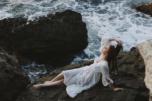 une femme dans une blanc robe pieds nus mensonges sur une pierre tenir par sa cheveux photo