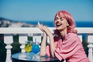 de bonne humeur femme avec rose cheveux séance à le table en plein air cocktail photo