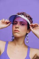 portrait de une sportif mode femme posant dans une violet des sports costume pour yoga et une transparent casquette sur une violet Contexte monochrome photo